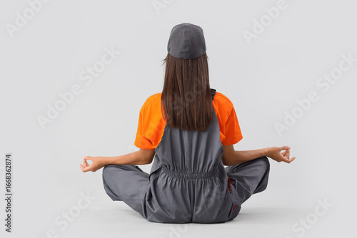 Female worker meditating on light background, back view