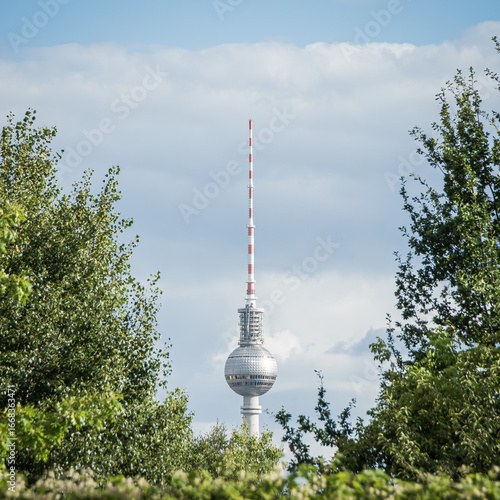 Berlin TV Tower framed by green trees, summer sky, Germany