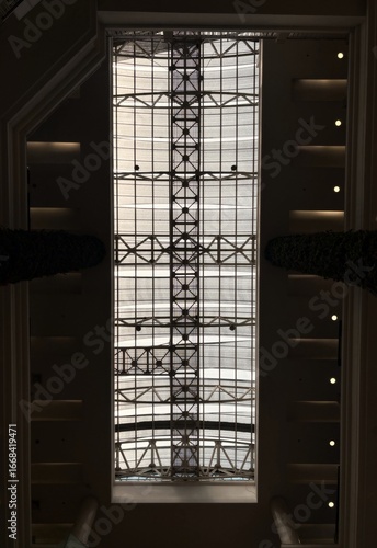 Architectural view of a modern skylight ceiling with geometric steel frame and glass panels. Interior roof structure allows natural light to pass through.