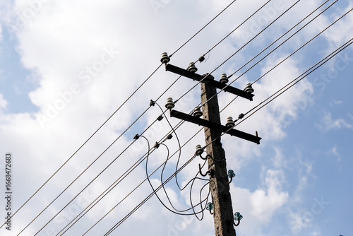 Concrete electric utility pole with multiple wires against blue sky background. Power line structure with insulators and cables. Infrastructure for electricity distribution and energy transmission.