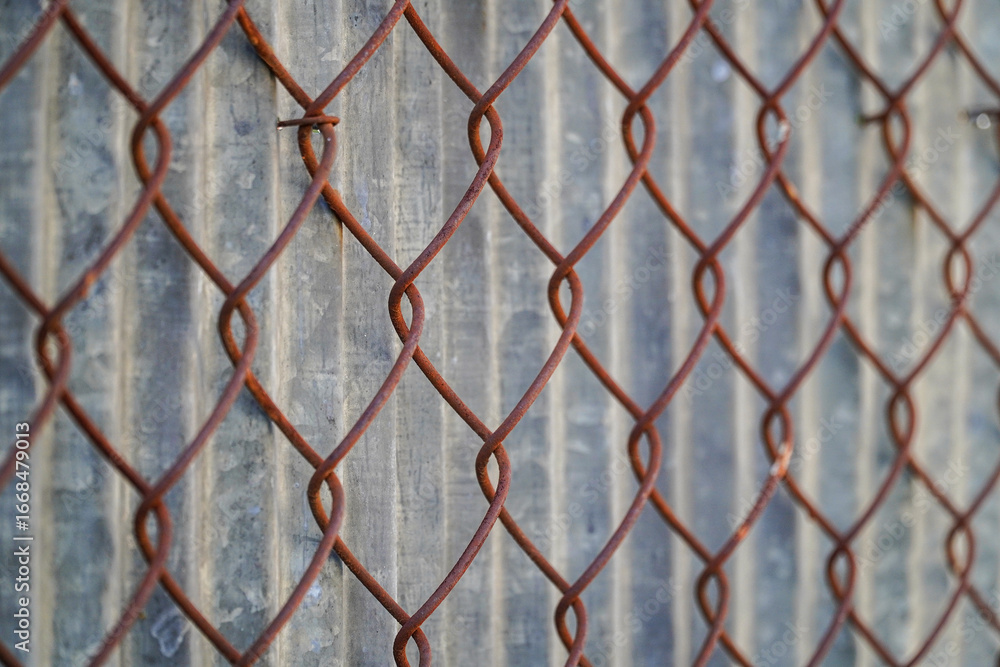 Naklejka premium A close-up perspective of a rusted wire fence against a textured background presents industrial textures and geometric patterns. Rust colored metal links creates visual interest.