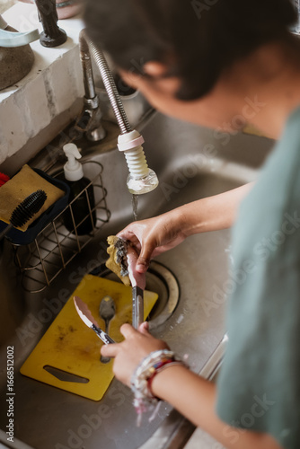 Teen female person washing kitchen utensils in the sink after finish cooking. motion blur.