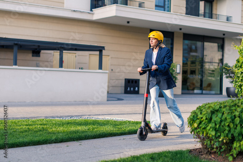 Young woman rides electric scooter on urban street wearing a yellow helmet