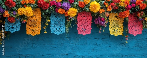 Vibrant day of the dead decorations with colorful flowers and papel picado against a textured blue wall backdrop