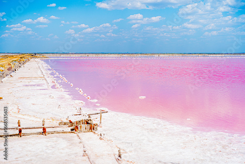 beautiful nature pink lake salt flats where salt is mined with soft pink water blue sky fluffy clouds and snow-white salt on the shore with a wooden structure bridge background beauty