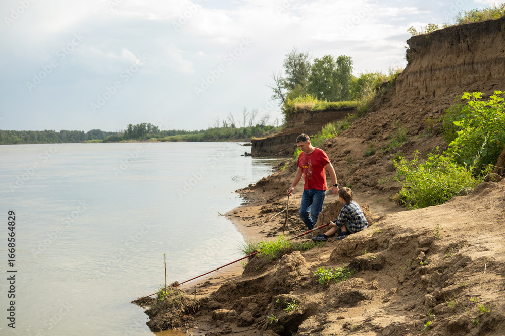 Fototapeta premium Grandfather is teaching a grandson fishing on the river beach.