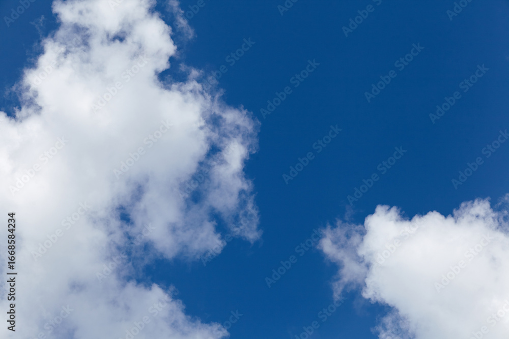 Obraz premium Bright blue sky filled with fluffy white clouds creating a serene atmosphere, ideal for backgrounds, designs, or nature-themed projects with ample copy space for text