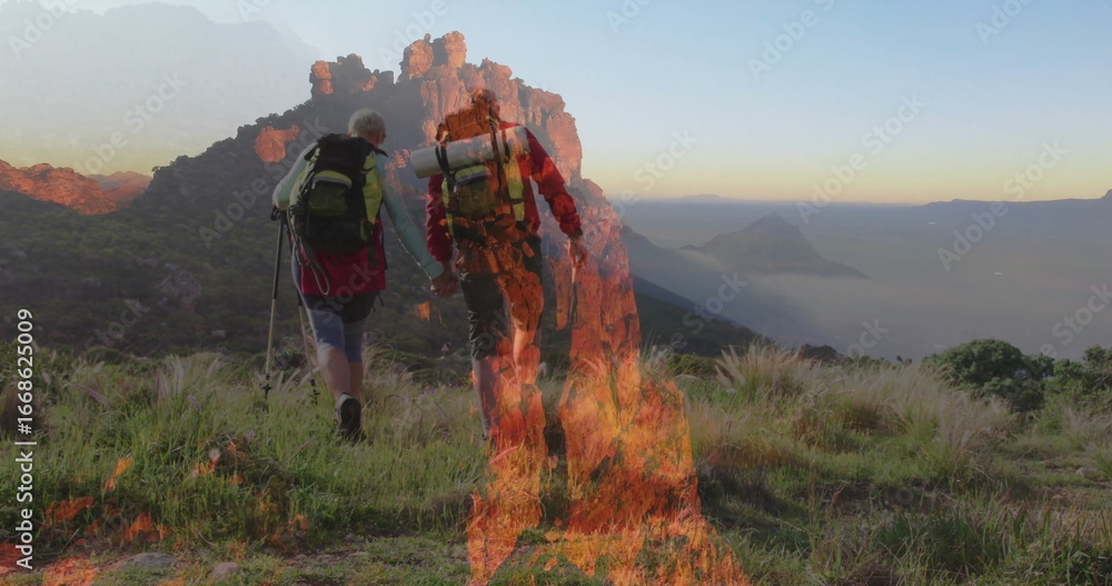Obraz premium Walking hiking couple climbing mountain slope at sunrise, with backpacks, poles, boots, flames