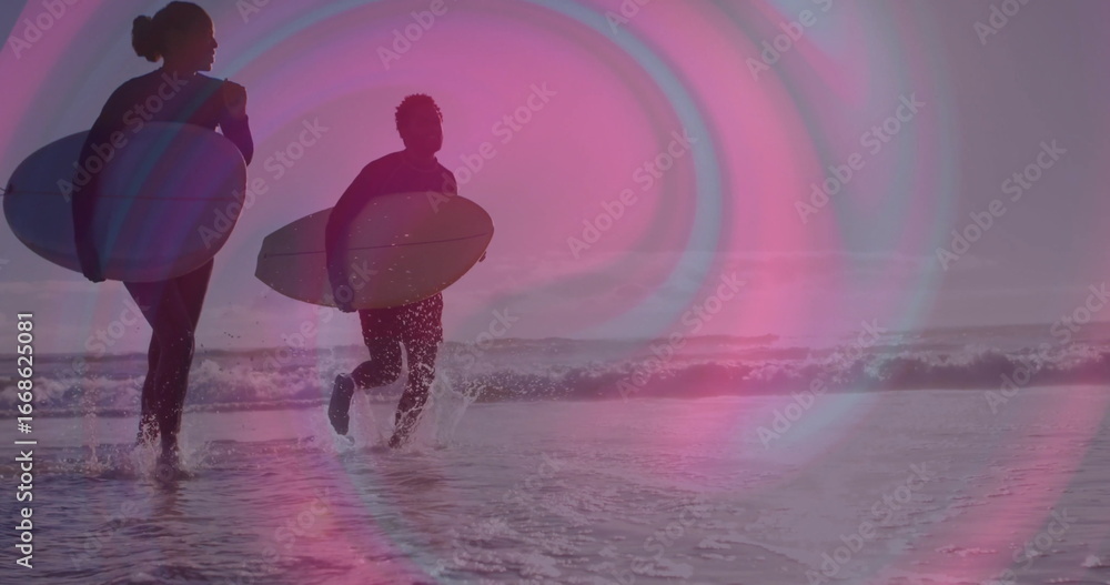 Fototapeta premium Walking duo of surfers carrying surfboards at sandy beach shoreline, with full-body wetsuits