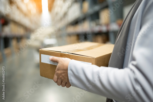 Rear view of Muslim female warehouse worker holding cardboard delivery box in warehouse