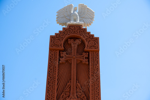 Tablou pe pânză Traditional Armenian Stone Cross with Intricate Carvings Against Blue Sky