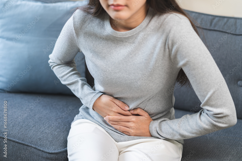 Fototapeta premium Sick asian young woman in pain, hand holding belly, stomach pain from food poisoning, girl hurt abdomen ache and digestive problem, gastritis or diarrhea. Health care inflammation, abdominal problem