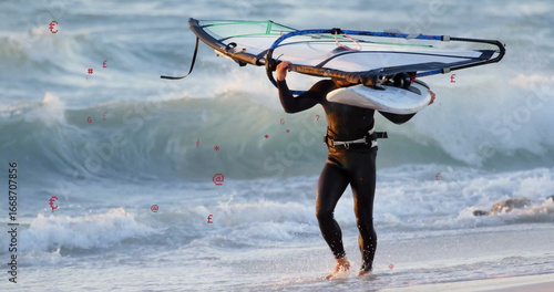 Vászonkép Walking man wearing wetsuit harness carrying windsurf board and sail rig on sand
