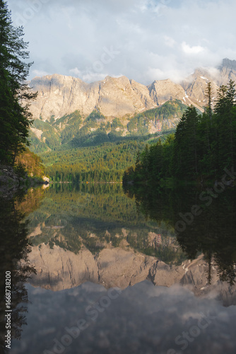 Peaceful alpine lake with crystal-clear reflection of mountains and surrounding forest under soft light. A tranquil and inspiring scene from Bavaria, Germany.