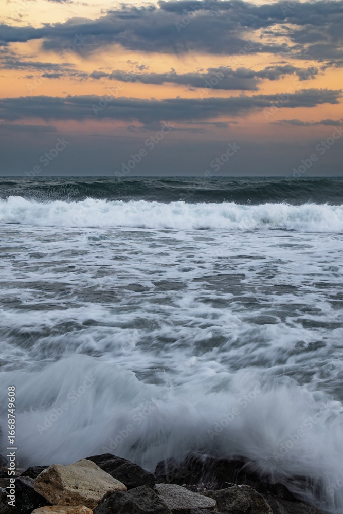 Fototapeta premium Ocean waves crashing against rocks at sunset