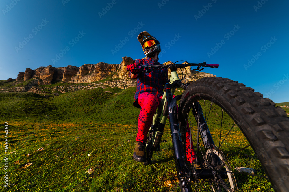 Obraz premium Front view wide angle of mountain bike and man in mountains against mountain range and hills with clouds and blue sky. Extreme sports concept, relaxation during training