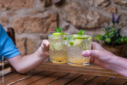 Two people sitting at a table making a celebratory toast with mojitos