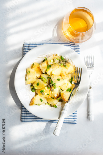 Overhead view of a bowl of traditional Greek potato salad (Patatosalata) on a table with cutlery, napkin and a glass of wine