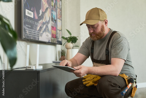 Foto Middle aged Caucasian man with beard wearing work uniform sitting near televisio