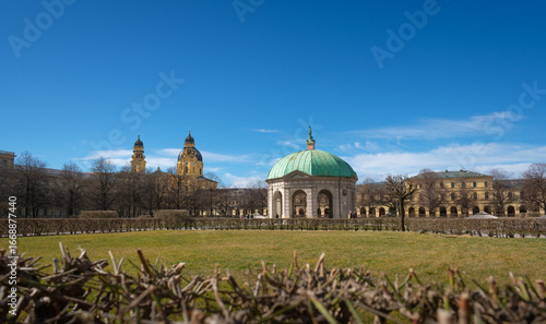 The Diana Temple (Dianatempel) in the Hofgarten, Munich, Germany, with the baroque towers of the Theatine Church in the background. A scenic blend of garden, culture, and historic architecture.