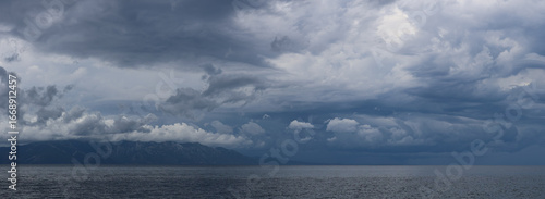 Stormy sky over mountains and sea. Dark dramatic clouds hang over the water surface, creating an atmosphere of tension and grandeur of nature. Podaca village, Makarska Riviera, South Dalmatia, Croatia