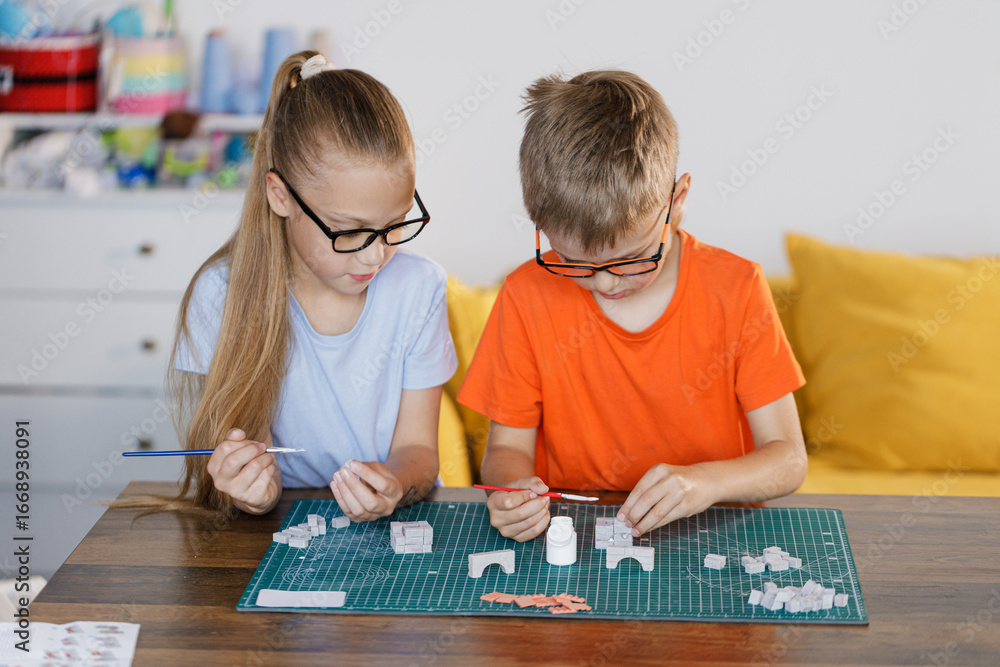 Fototapeta premium Boy and girl in glasses assembling constructor at school desk. Educational STEM activity for children developing creativity, teamwork, and problem-solving skills.