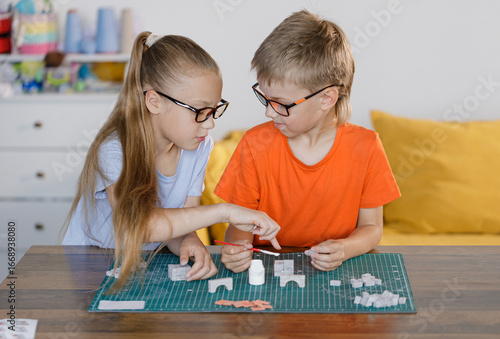 Boy and girl in glasses assembling constructor at school desk. Educational STEM activity for children developing creativity, teamwork, and problem-solving skills.