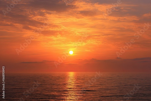 Fiery sunset over a calm ocean, the sun a bright orb casting an orange glow on the water and clouds
