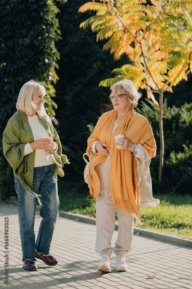 Obraz premium Two senior women walking and talking in a park during autumn