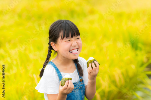 田んぼの前でおにぎりを食べる女の子