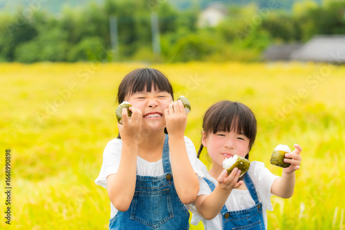 田んぼの前でおにぎりを持つ姉妹
