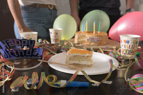 Festive birthday celebration with cake, balloons, candles, and colorful decorations on a table. Slice of cake in the foreground. Perfect for themes of family, parties, and joyful moments.