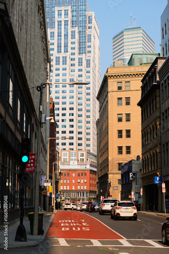 Boston city street of Chinatown district, lined with historic and modern buildings, showing a red bus and bike lane leading into the busy downtown skyline.