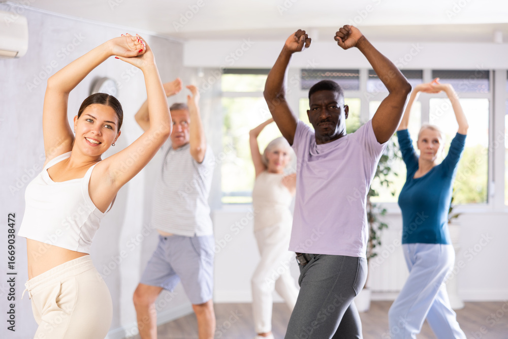 Naklejka premium Positive smiling young female dance instructor practicing moves of passionate flamenco with mixed age multiracial group of mature women and men