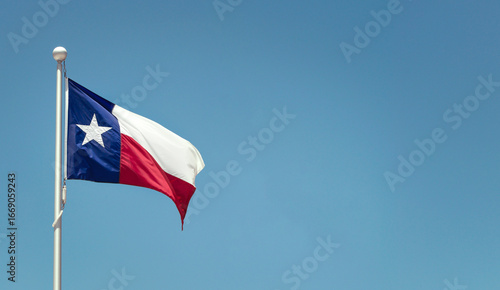 Texas State flag on the pole waving in the wing against bright blue sky 