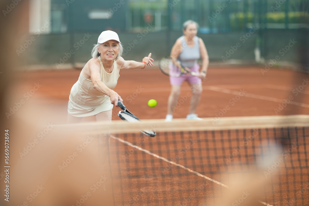 Obraz premium Elderly women in doubles playing tennis on tennis court
