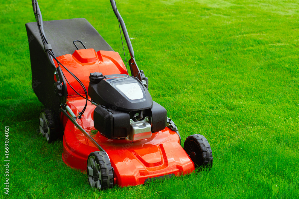 Close-up of a red lawn mower on fresh green grass. Concept gardening, landscaping, and lawn maintenance. Close-up of a red lawn mower on fresh green grass. Concept gardening, landscaping, and lawn maintenance.