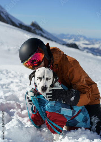Dog in winter jacket with owner on snowy mountain
