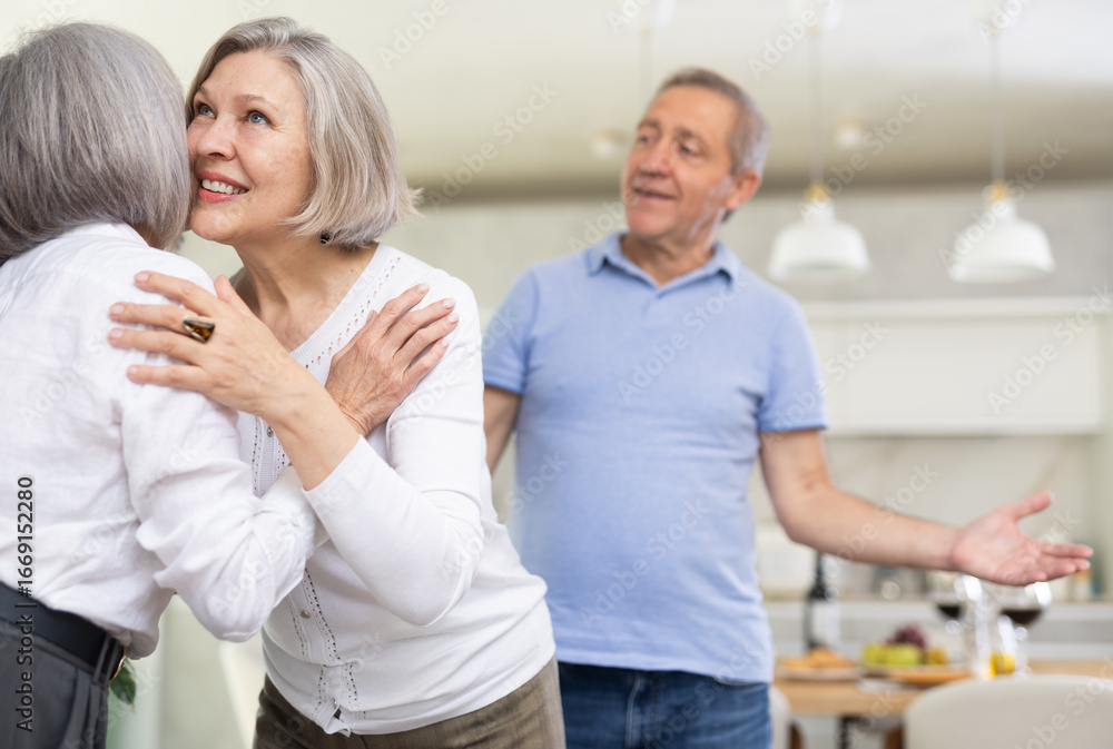 Fototapeta premium Two elderly women friends hugging in kitchen at home