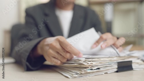 Close-up of businessperson's hands sorting a messy stack of papers on desk. Concept of office work, paperwork, stress, and information overload.