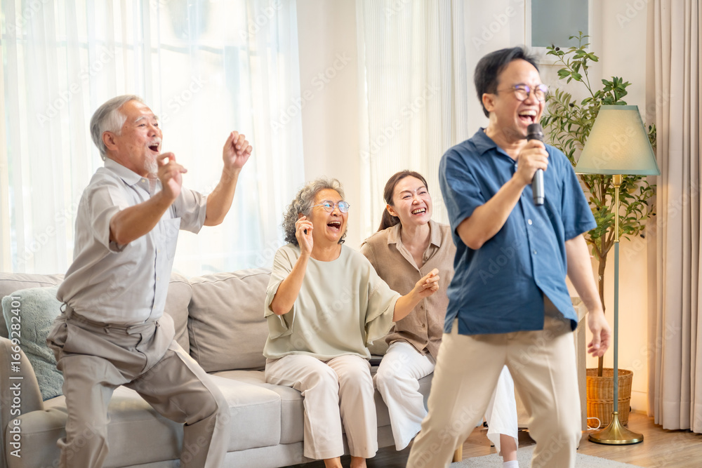 Obraz premium Happy Asian family senior parents and adult child spending time together at home. Healthy elderly father and mother enjoy and fun singing karaoke song dancing with daughter and son in living room.