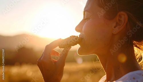 Woman enjoying fresh baked biscuit, backlit by sunset in golden field