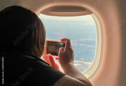 Unrecognizable woman traveler taking photos with her mobile device from an airplane’s window while flying. 