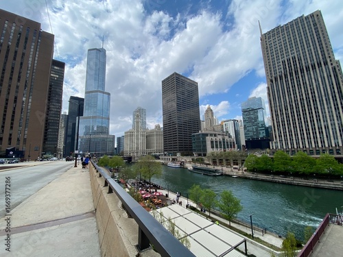 A peaceful view along the Chicago Riverwalk, with people strolling along the path. The image captures the serene waterway and the towering skyscrapers that line the banks, creating a sense of urban tr