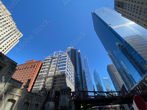 A low-angle view of Chicago's skyline, with multiple glassy skyscrapers reaching towards a vibrant blue sky, highlighting the city's modern architecture and verticality.