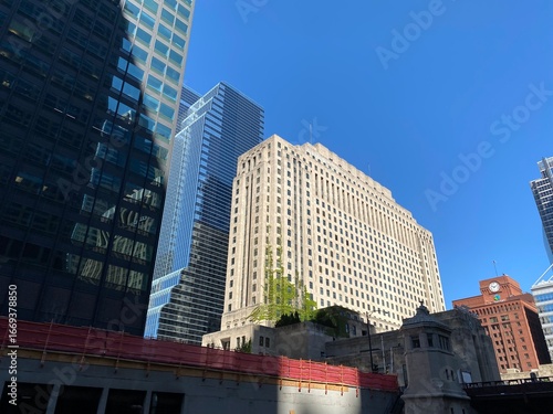 Looking up at the impressive architecture of a towering skyscraper with a distinctive facade and numerous windows, showcasing the scale and density of a bustling financial district under a bright sky.
