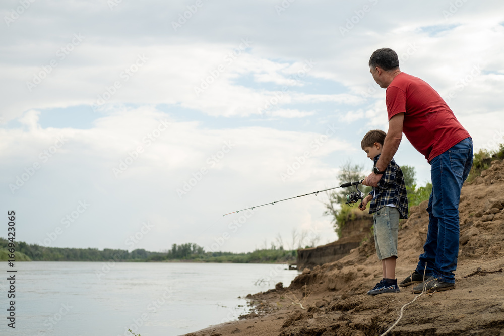 Grandfather is teaching a grandson fishing on the river beach. Grandfather is teaching a grandson fishing on the river beach.