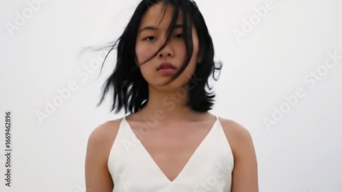 A serene portrait of a woman in a white dress standing against a minimalistic backdrop