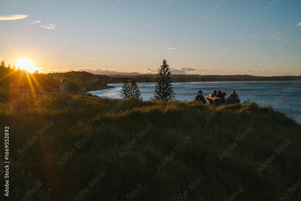 Obraz premium Friends enjoying scenic sunset overlooking ocean from grassy hilltop