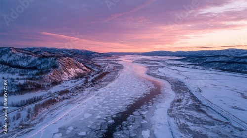 Frozen river winding through snowy mountains at dawn